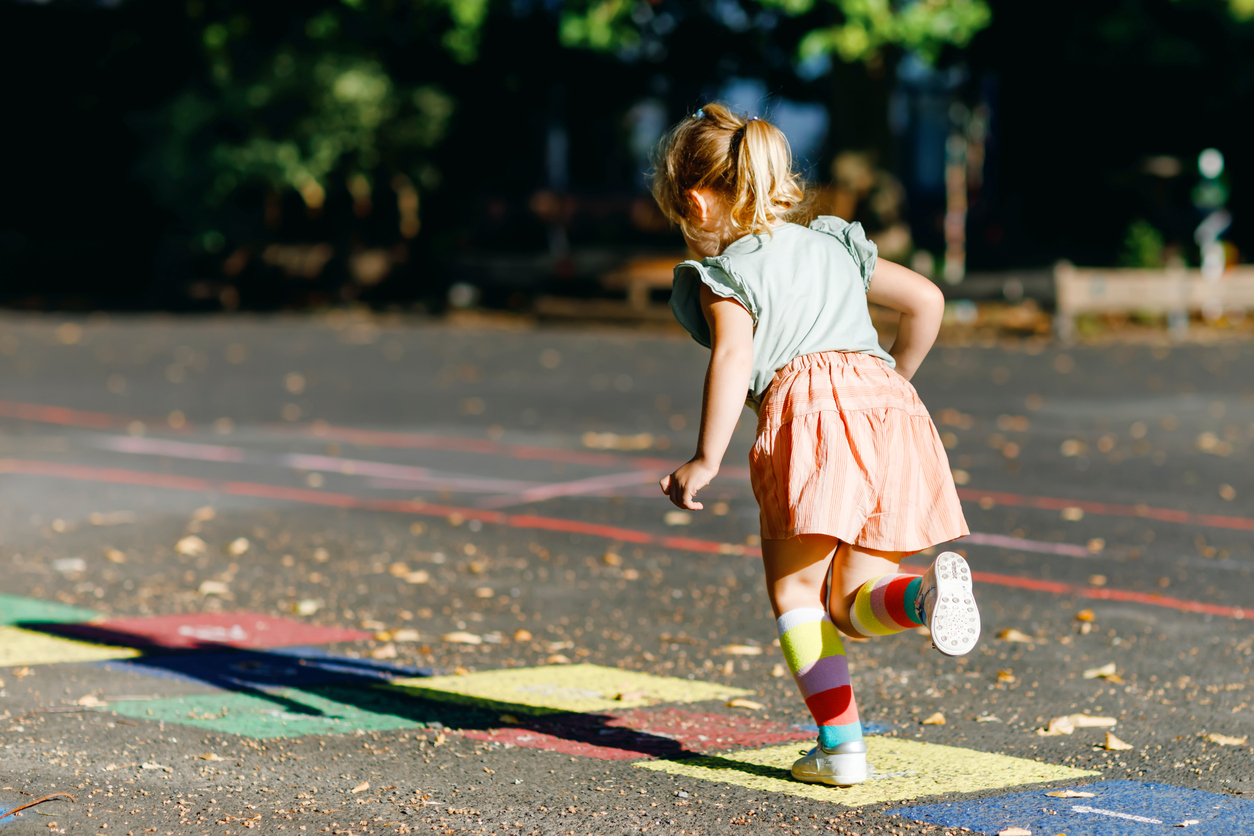Mädchen springt auf farbigen Spielfeldern im Freien.
